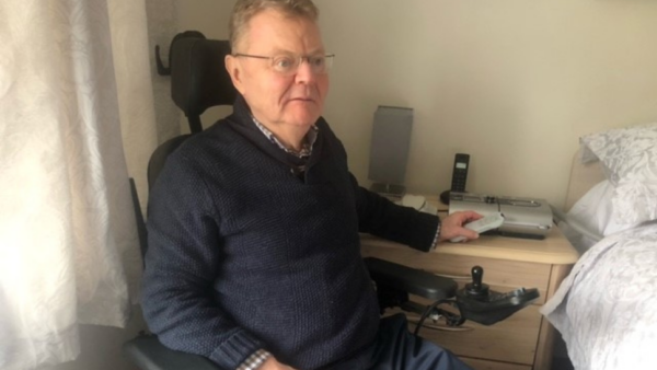A man sits beside a bed holding a remote