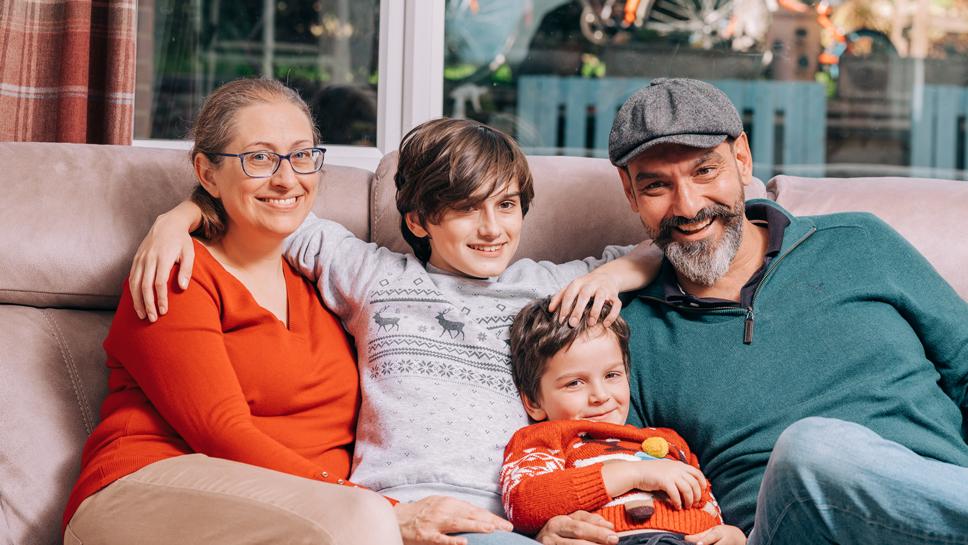 A family of four sit on a sofa and smile at the camera