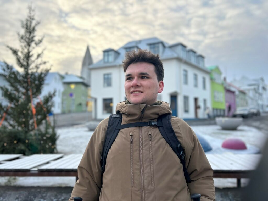 A man poses in an icey town square. A christmas tree is to his right,
