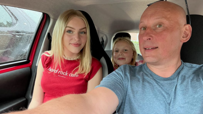 A smiling family of three sit in a car and take a selfie