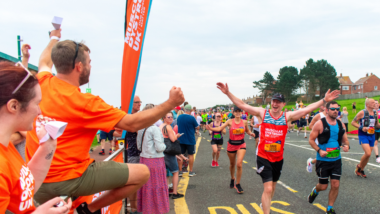 A man running in a race wearing a MDUK sports top with his hands raised in celebration