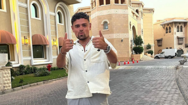 A man stands infront of an impressive building with two thumbs up