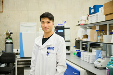 A scientist stands in a lab looking at the camera