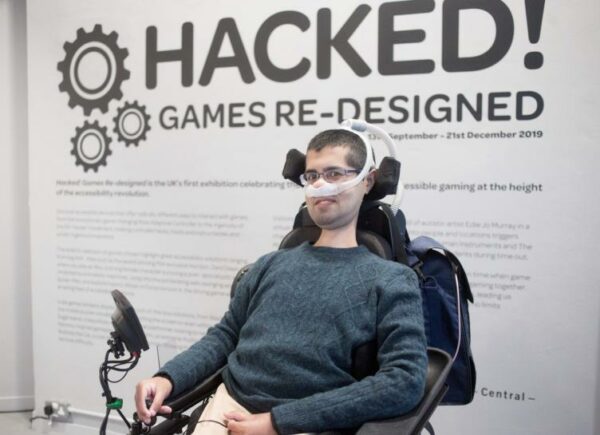 A man sits infront of a giant sign saying hacked