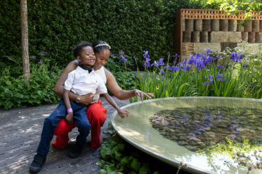 A happy women and boy crouch by and interact with a water feature at Chelsea Flower Show in MDULK's garden.