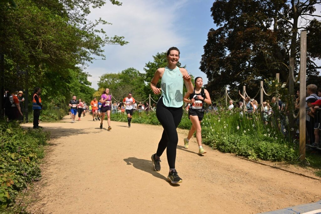 A woman running happily on a track. She has a teal running vest on.