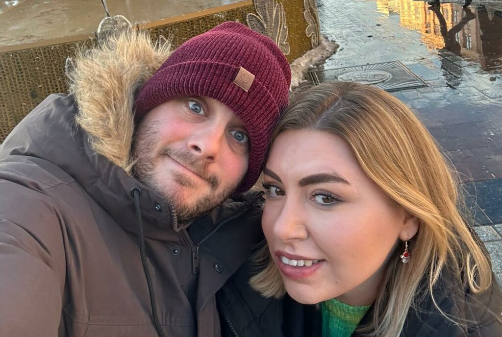 A young couple pose together touching heads in a cold climate in an urban backdrop.