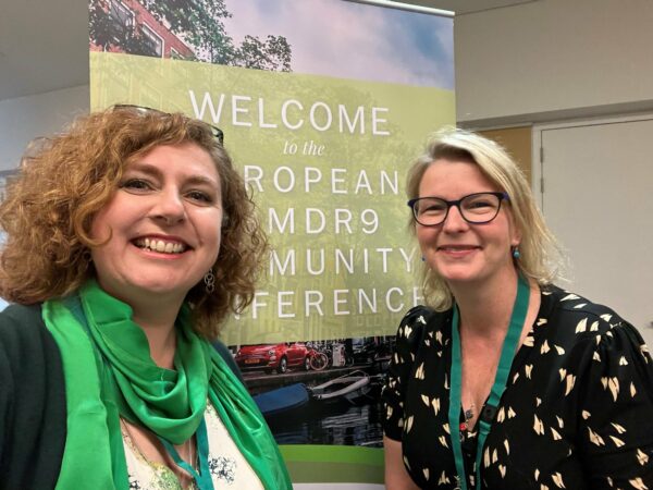 Two women stand by a pop-up banner at a conference