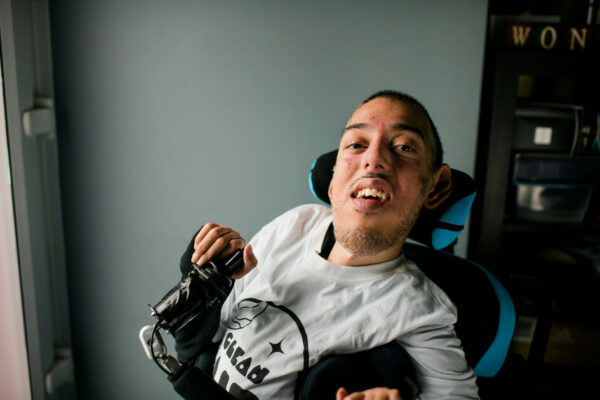 A man in a wheelchair with a grey top on a light blue wall in the background