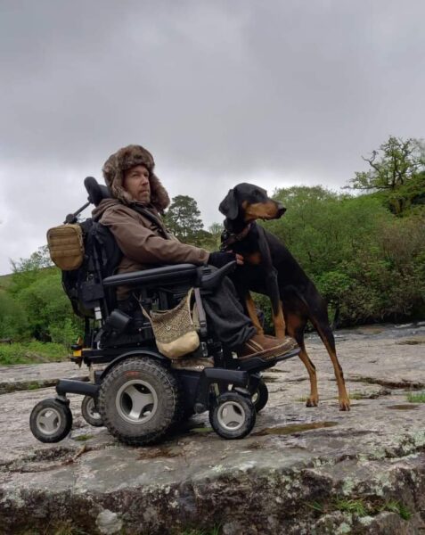 A man in a wheelchair with a warm hat on and a dog