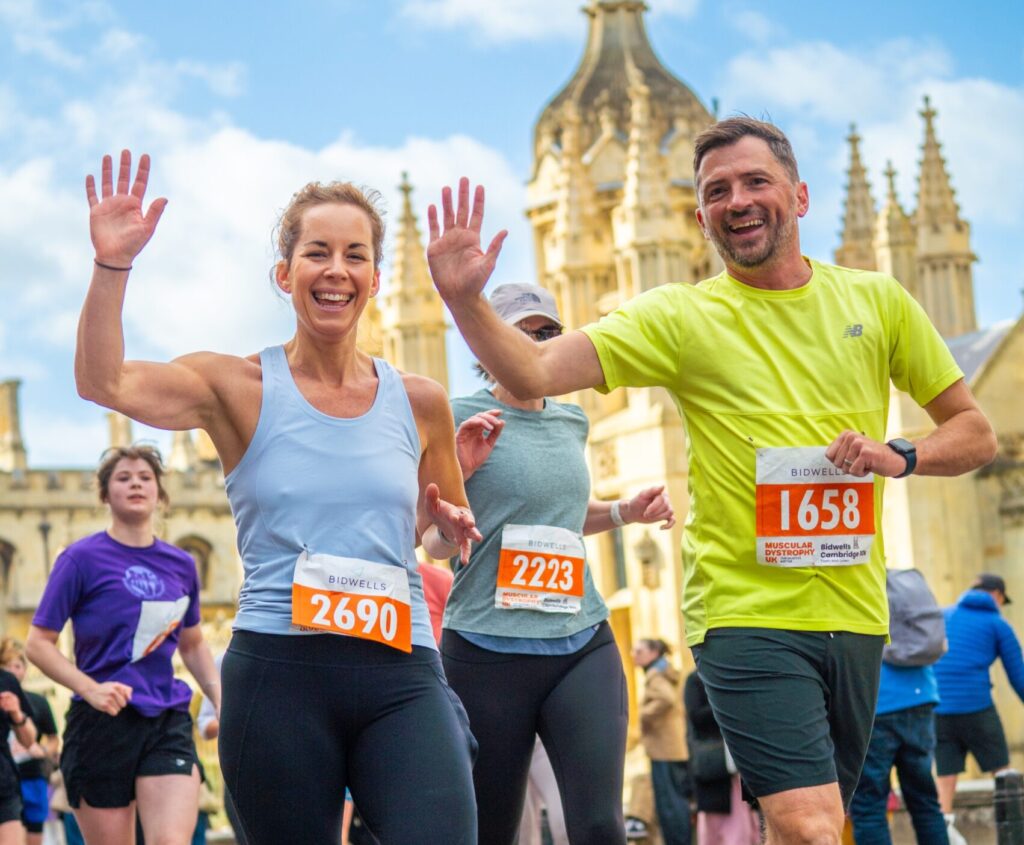 A pair of runners smile while waving at the camera during the Cambridge 10k.