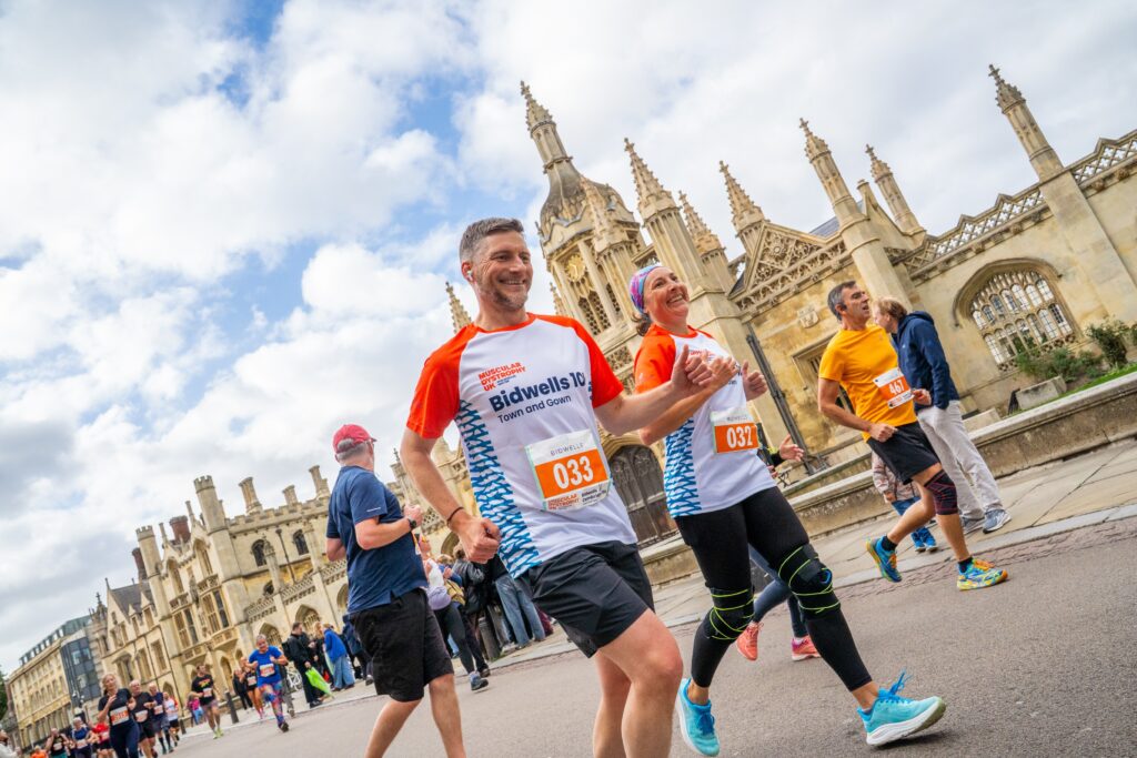 A group of runners smile as they run past a historic building during the Cambridge 10k.