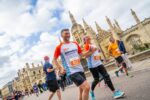 A group of runners smile as they run past a historic building during the Cambridge 10k.