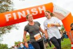 Two individuals laugh and smile as they cross the finish line of the Cambridge 10k.