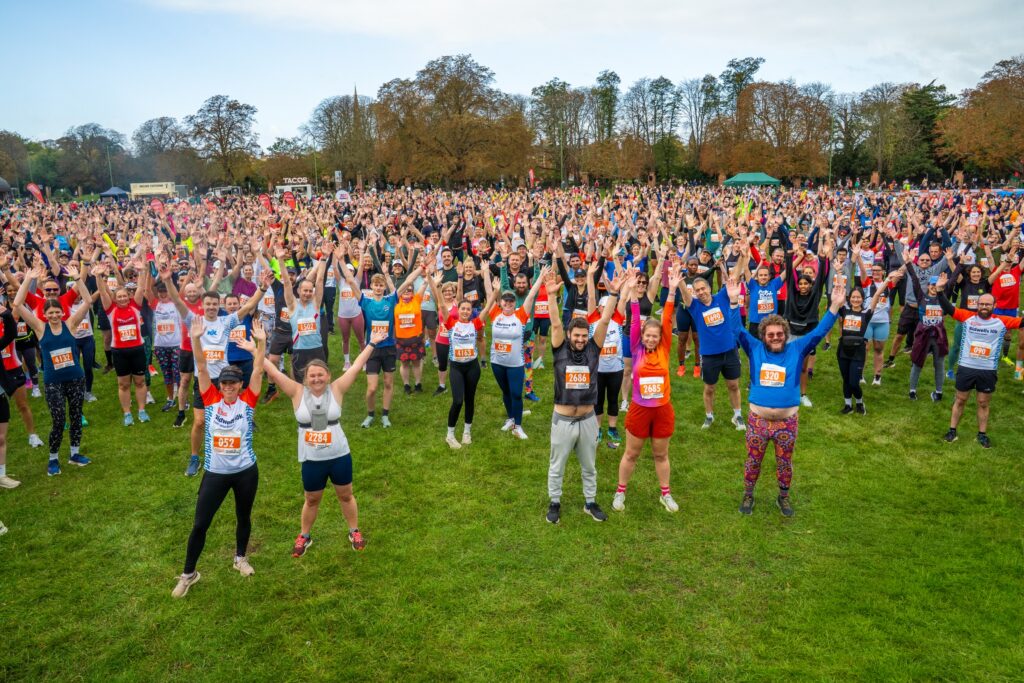 A large group of runners stand with their arms raised before completing the Cambridge 10k.