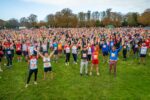 A large group of runners stand with their arms raised before completing the Cambridge 10k.