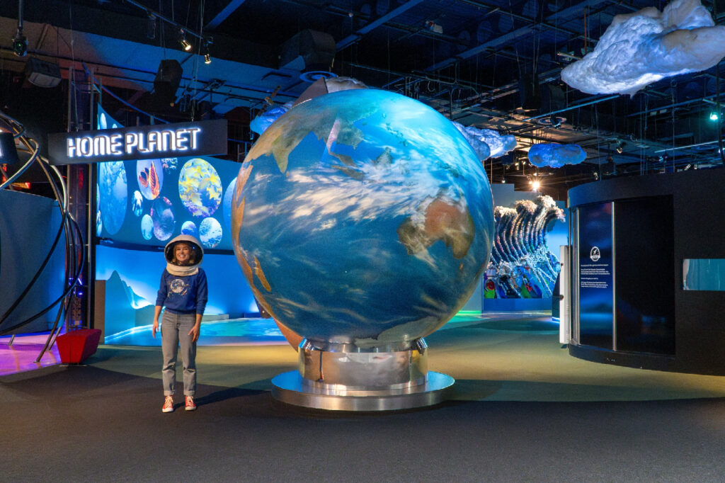 Woman stands in space centre next to a model of a globe.