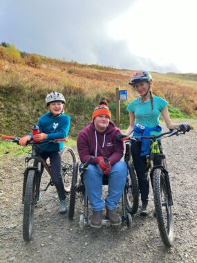 Two people on bicycles are sat next to a man in a wheelchair