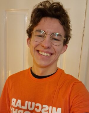 A man in a muscular dystrophy uk orange top smiles at the camera