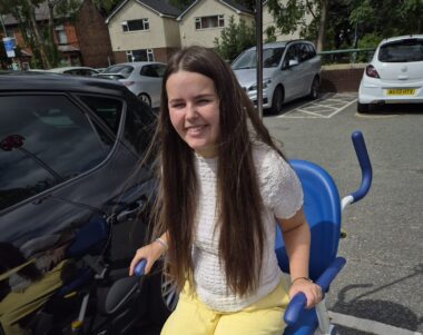 A girl in yellow trousers sits in a chair outside