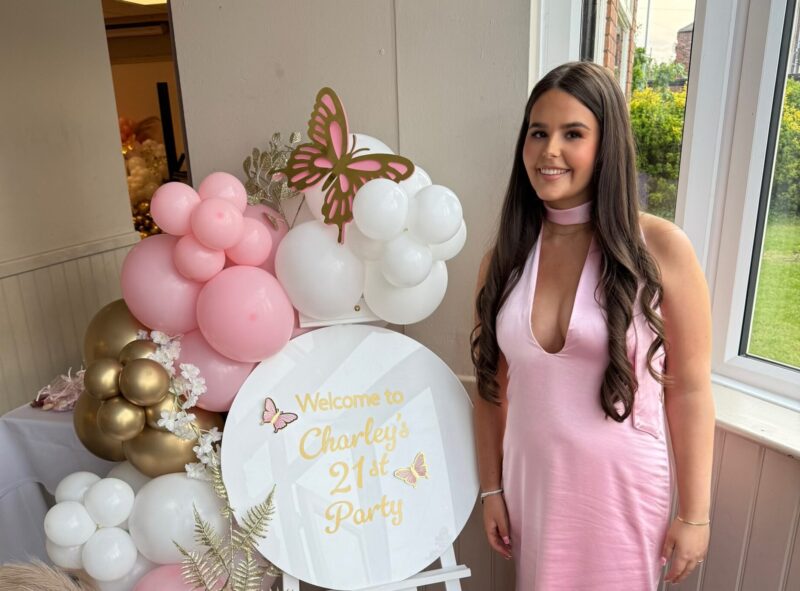 A girl in a pink dress stands next to balloons