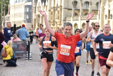 A person running in an orange top holds their hands in the air.