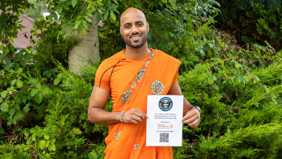 A picture of Krish wearing his Grandmother's orange Sari holding a certificate about his world record attempt