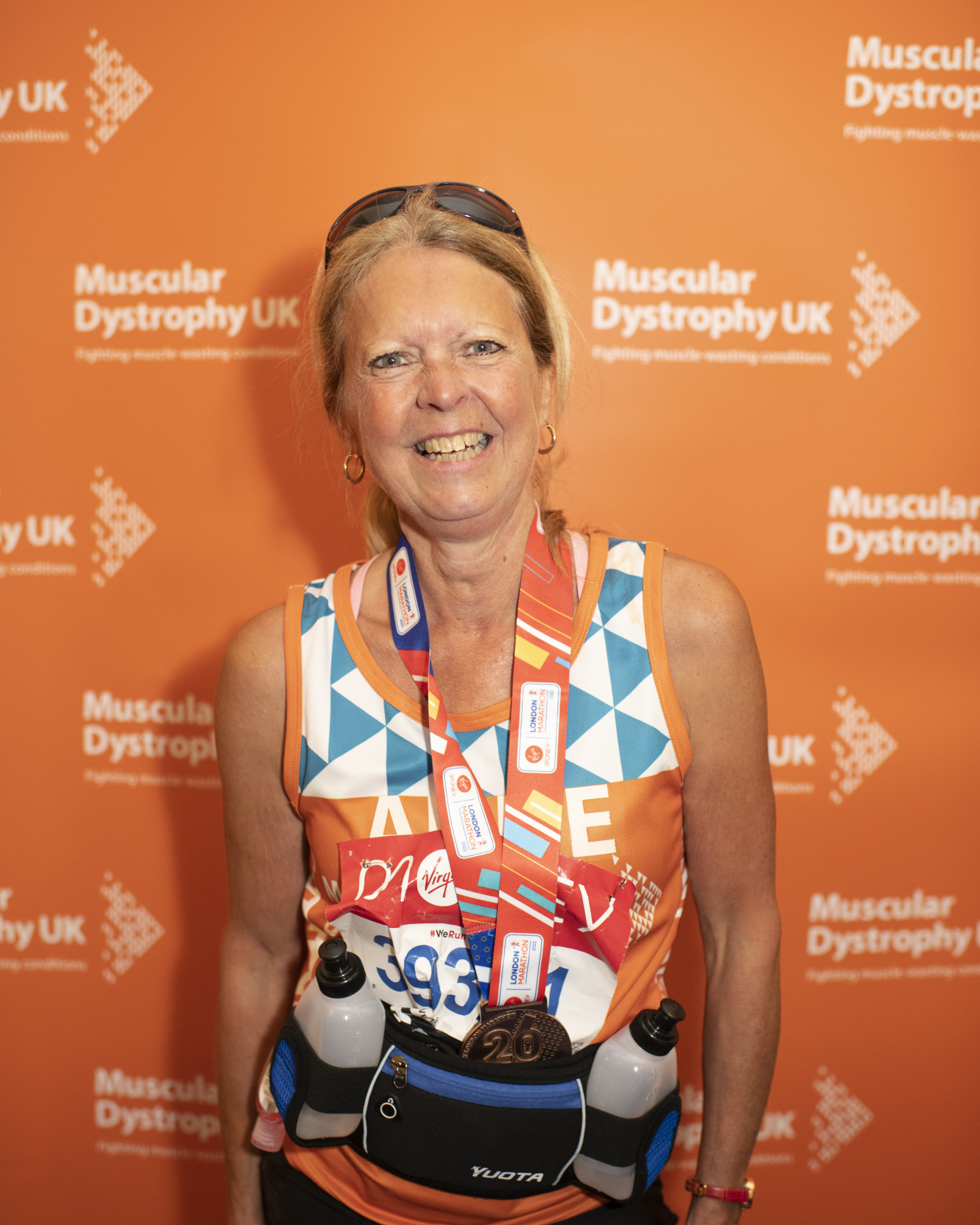 Anne Peterson is stood in her Team Orange jersey, against an MDUK backdrop after running the London Marathon