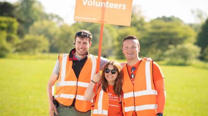 Three MDUK volunteers standing together with a sign saying 'Volunteers' at the Oxford Town & Gown.
