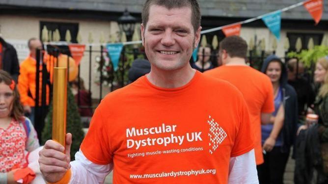 Martin Hywood in MDUK orange t-shirt fundraising for MDUK with bunting and people in the background