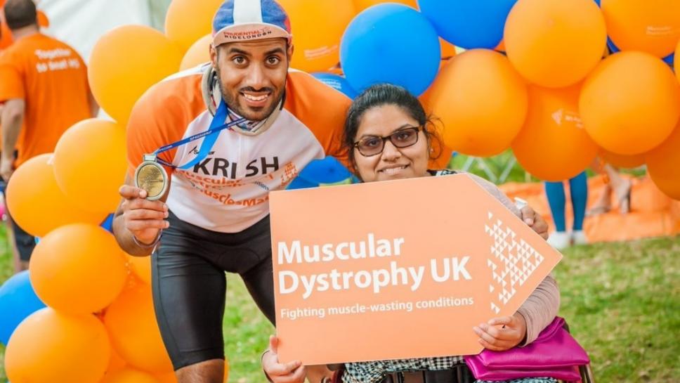 Image of Krish holding his medal and Anjali holding an MDUK poster in front of a balloon arch