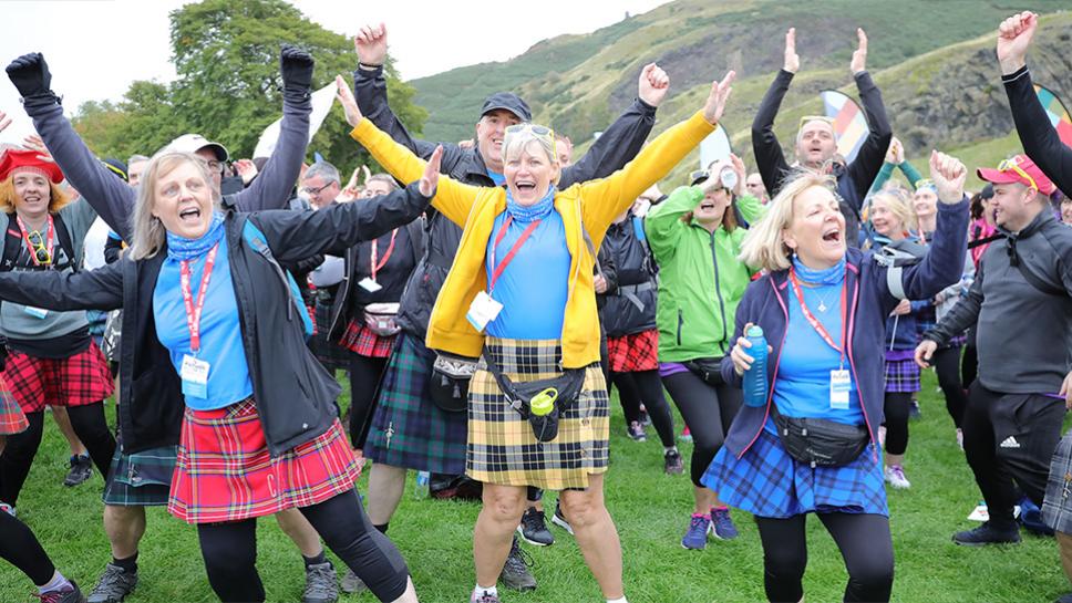 Crowd of people wearing kilts, laughing with their arms in the air