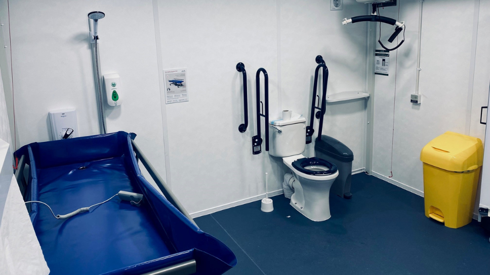 An image of the inside of a Changing Places Toilet at Elland Road Stadium. In the image you can see a toilet, a hoist, an adult changing table.