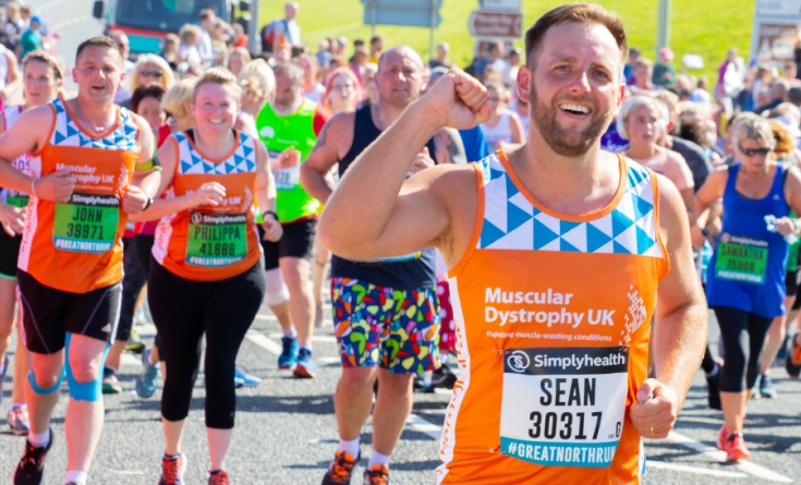 This photo shows 1 runner for Muscular Dystrophy with his fist up in the air smiling and 2 other runners for MDUK in the distance looking towards our #TeamMDUK cheer point