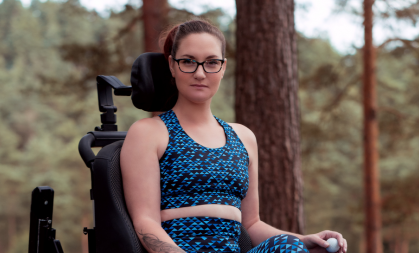 Image of Gems sitting in her wheelchair, wearing her Tikiboo workout clothing with trees in the background