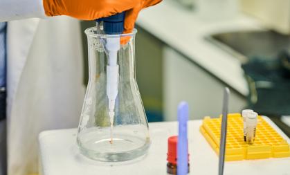 Research image of a scientist in orange gloves working with a beaker
