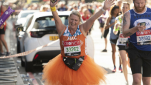 Team Orange runner wearing an orange tutu, smiling, with her arms in the air