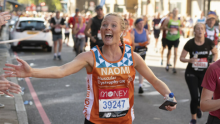 A Team Orange runner smiling and reaching their arm out as they run past