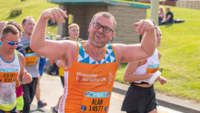 A Team Orange runner smiling with his arms in the air as he runs past