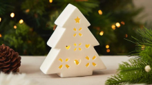 A white ceramic Christmas tree ornament. Led lights up the tree through cutout stars in its design. 