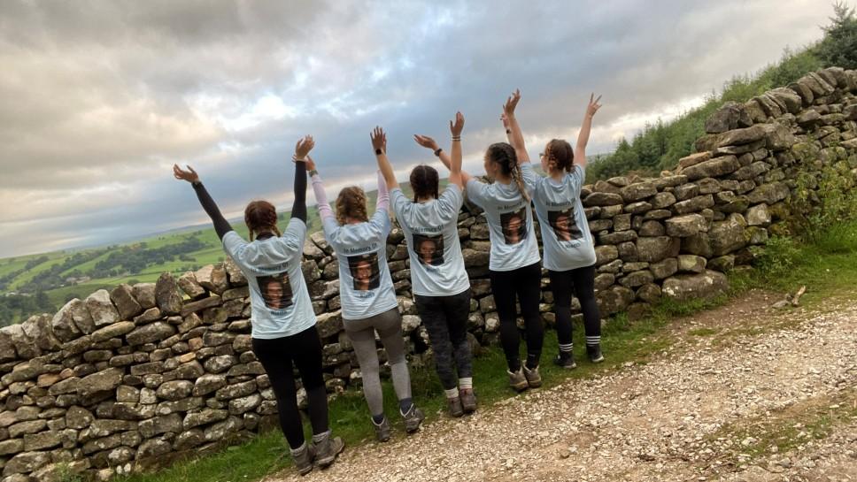 Five women throwing there hands into the air in the countryside